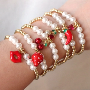 Detail of layered gold and pearl bracelets with red fruit charms on a woman's wrist