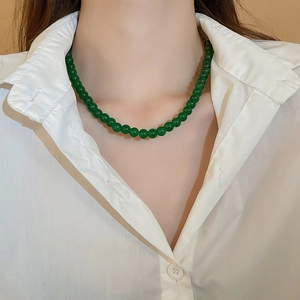 Détail d'un collier en perles de verre vert émeraude porté sur une chemise blanche