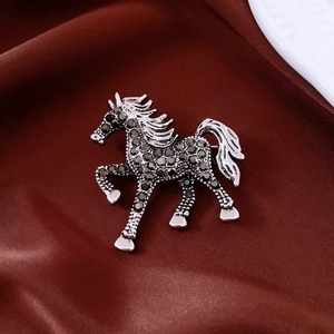 Detailed close-up of a vintage horse brooch with grey rhinestones on silk background