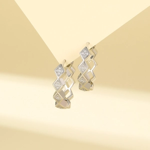 Macro shot of silver rhombic hoop earrings with pavé-set zircons on yellow background