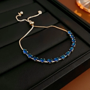 Detail of adjustable gold chain bracelet with marquee-cut navy blue gemstones on black tray