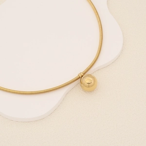 Macro shot of a golden choker necklace featuring a polished spherical pendant on a white stand