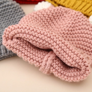 Close-up of thick knit winter baby hat with soft white pompom and elastic texture