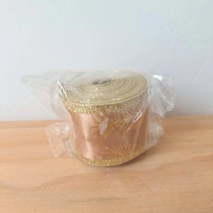 Detailed view of champagne gold glitter ribbon roll with floral leaf patterns in packaging