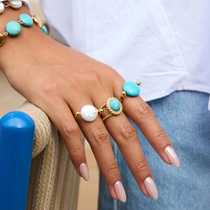 Close-up of stacked gold rings with turquoise and pearls worn with a matching bracelet
