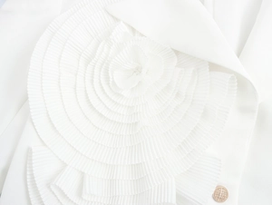 Detail of elegant white blazer featuring 3D spiral pleated flower and gold button