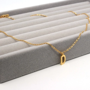 Macro shot of gold stainless steel necklace with letter D pendant on velvet