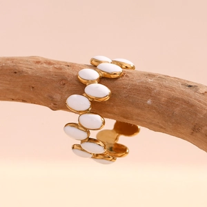 Detail of 18K gold-plated wavy ring with white enamel ovals on a natural branch