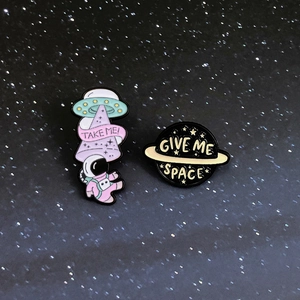 Close-up of UFO and planet enamel pins with Take Me and Give Me Space text designs