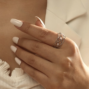 Close-up of a silver crisscross open ring with small pearls worn on a model's finger