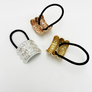 Close-up of three elastic U-shaped hair ties with textured gold, silver, and rose gold metal buckles