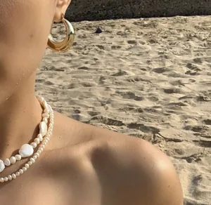 Look de exterior con pendientes de aro dorados y collares de perlas de doble capa
