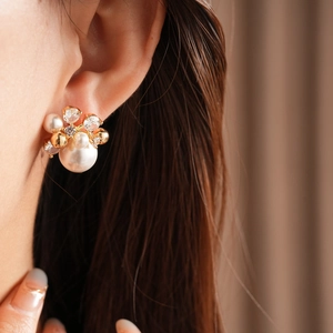 Close-up of gold-plated flower stud earrings with pearls and sparkling zircons on model