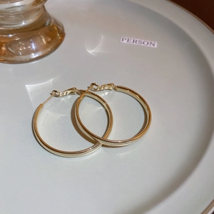 Minimalist gold hoop earrings displayed on a white tray with elegant lighting