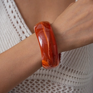 Detail of wide orange acrylic bangle with marble pattern worn by a model