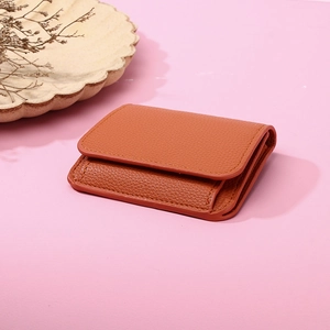 Detailed view of an orange pebble leather cardholder with fine stitching on pink surface