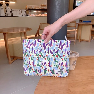 Detail of the tulip floral canvas cosmetic bag being held over a wooden cafe table