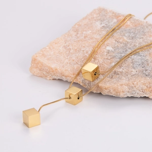 Minimalist gold square pendant on sleek snake chain necklace over natural stone