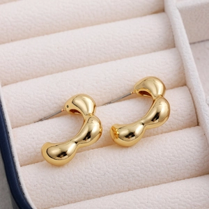 Close-up of golden irregular fluid-shaped stud earrings on white velvet jewelry tray
