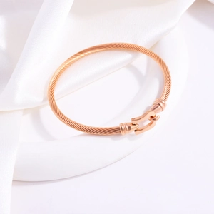 Rose gold twisted rope bangle with horseshoe buckle on white silk background