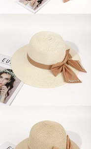 Detail of wide-brim straw hat with brown satin bow and pearl accents for sun protection