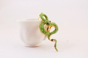 Detail of a gold snake keychain with green rhinestones hanging on a white ceramic cup