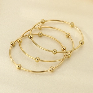 Macro detail of three stacked gold bangle bracelets with decorative polished metal beads