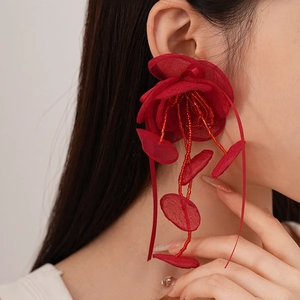 Détail des boucles d'oreilles fleur rouge avec pompons perlés et texture mousseline
