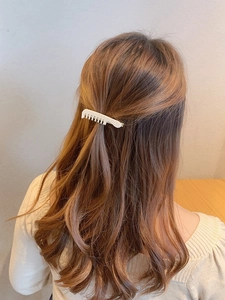 Detail of a white pearl bow hair clip worn on long brown hair from a back view