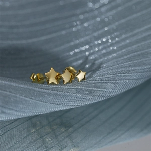 Macro shot of three graduated gold star studs on a textured silk background