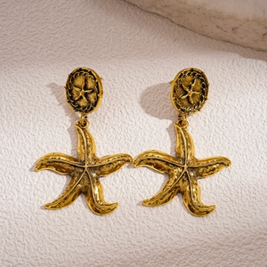 Vintage geometric starfish gold earrings with textured metal finish on white stone