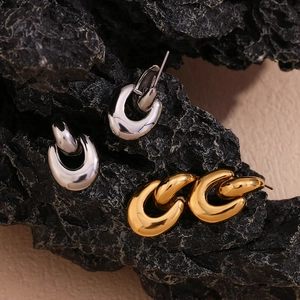 Detailed shot of polished gold and silver U-shaped chain earrings on dark textured rock