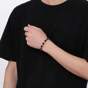Detail view of men's black and silver woven leather bracelet on wrist with a metal bead clasp