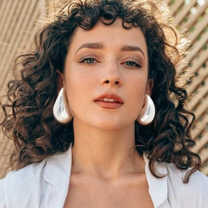 Close-up of large silver water drop earrings worn by a model in a white shirt