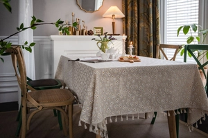 Detail of beige linen tablecloth with white daisy pattern and elegant fringe edges