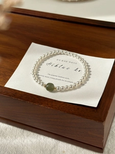 Macro detail of white pearl bracelet featuring an olive green bead and gold accents