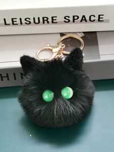 Close-up of black plush cat ball keychain with green eyes and golden metal clasp