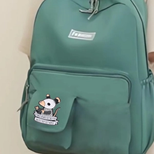Cartoon opossum enamel pin on a green backpack featuring motivational quote metal badge