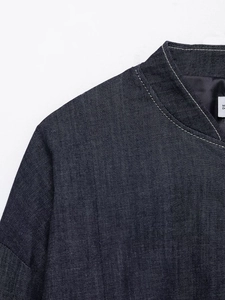 Detail shot of navy denim bomber jacket showing white contrast stitching and fabric texture