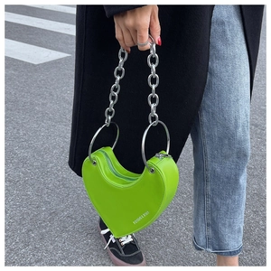 Street style shot of a green heart-shaped handbag with silver chain and metal handles