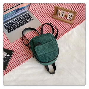 Detail of dark green corduroy backpack with front flap pocket on a cozy checkered setting