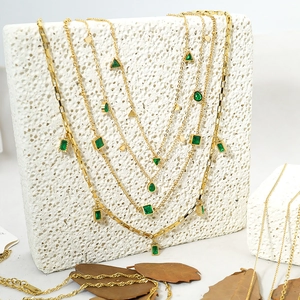 Detail of layered gold necklaces with emerald green rectangle and pear-shaped pendants