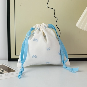 Detailed close-up of cream canvas drawstring bag with light blue bow patterns and satin ribbon