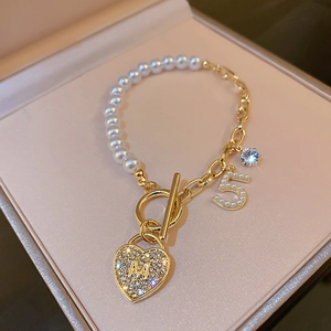 Macro shot of gold-plated pearl bracelet with heart-shaped M pendant and number 5 charm