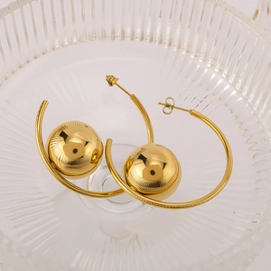 Close-up of golden C-shaped hollow earrings with large sphere bead in a glass bowl
