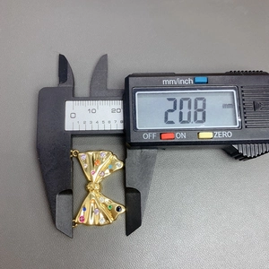 Digital caliper measuring the 20.8 mm width of a gold bow pendant with colorful stones