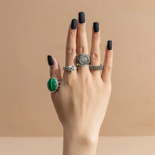 Detail view of silver punk rings set featuring skull and green stone on model's hand