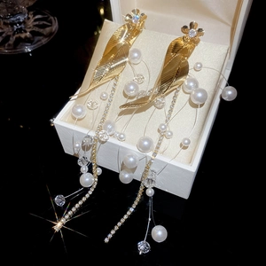 Macro detail of leaf-shaped gold earrings with sparkling fringe and white pearls