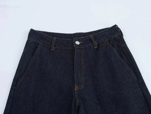 Détail d'un pantalon en jean bleu foncé avec coutures orange et bouton en métal argenté