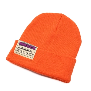 Detail of orange beanie featuring boarding pass patch with HKG to NYC flight design